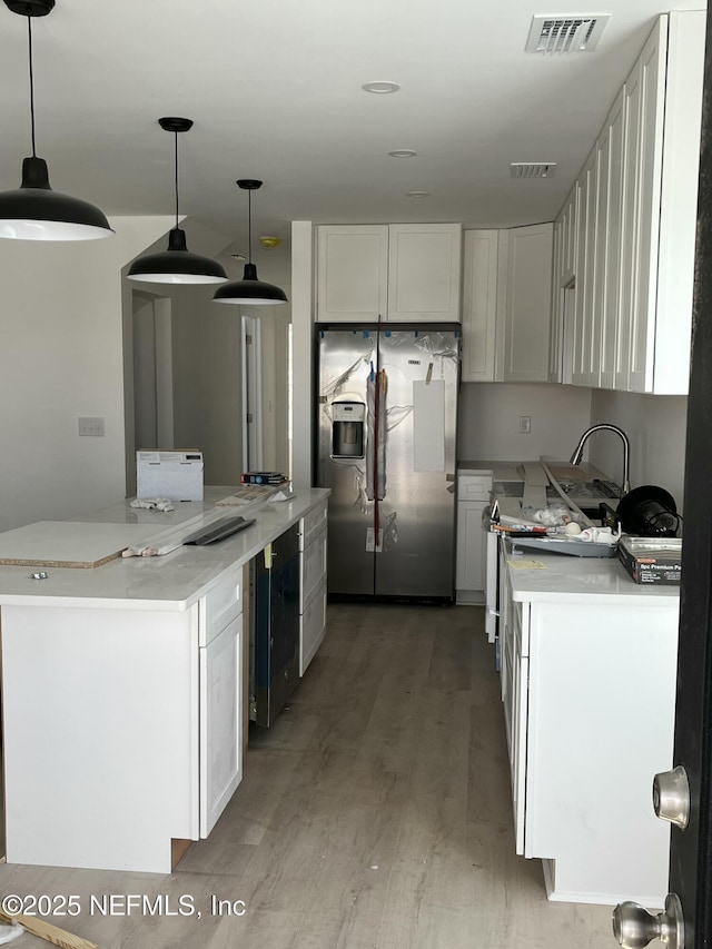 kitchen with stainless steel fridge, visible vents, white cabinets, and pendant lighting