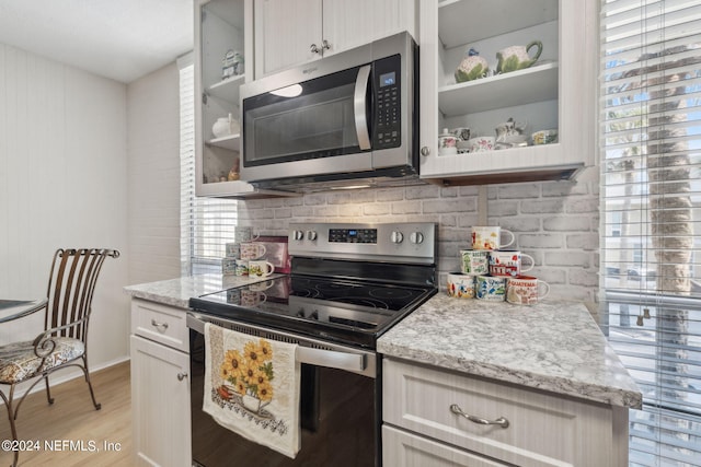 kitchen with appliances with stainless steel finishes, a wealth of natural light, light stone countertops, and light hardwood / wood-style floors