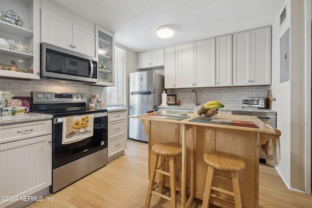 kitchen featuring white cabinets, a center island, light hardwood / wood-style flooring, appliances with stainless steel finishes, and a kitchen bar