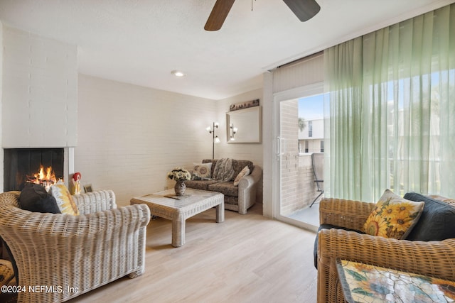 living room with light wood-type flooring, ceiling fan, and a fireplace