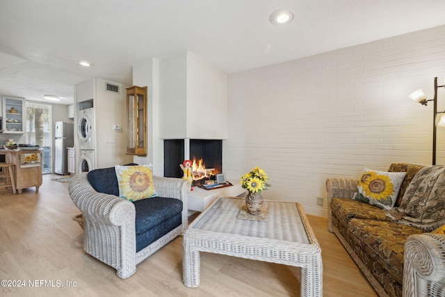 living room featuring stacked washer / dryer, light hardwood / wood-style flooring, and brick wall