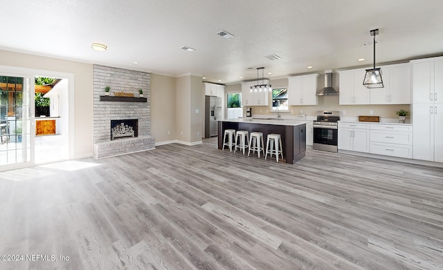 kitchen featuring wall chimney exhaust hood, appliances with stainless steel finishes, a center island, hanging light fixtures, and white cabinetry