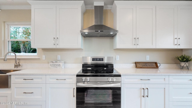 kitchen with stainless steel range oven, light stone counters, white cabinetry, wall chimney range hood, and ornamental molding