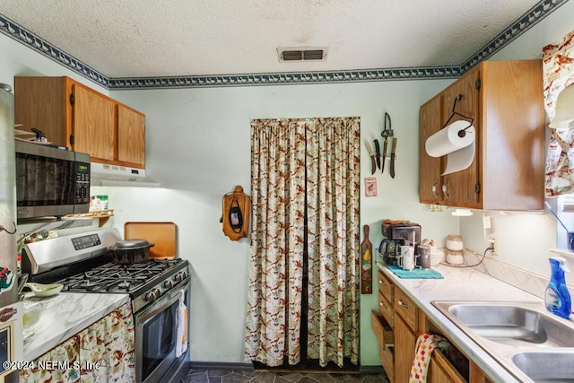 kitchen with a textured ceiling, visible vents, light countertops, under cabinet range hood, and appliances with stainless steel finishes