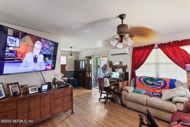 living room featuring a wall mounted air conditioner, a textured ceiling, light wood-style flooring, and a ceiling fan