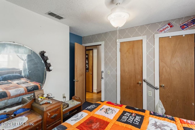 bedroom with visible vents, a textured ceiling, and wallpapered walls