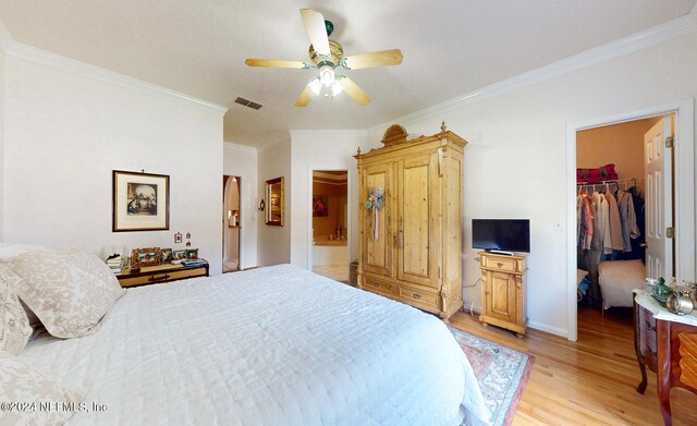 bedroom with ornamental molding, light hardwood / wood-style flooring, ceiling fan, a closet, and a spacious closet