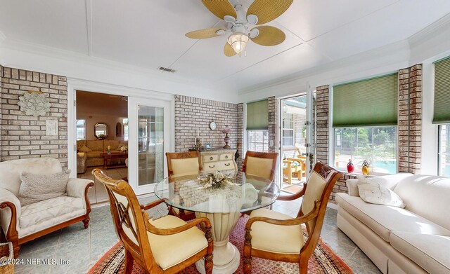 tiled dining area with ornamental molding, brick wall, and ceiling fan