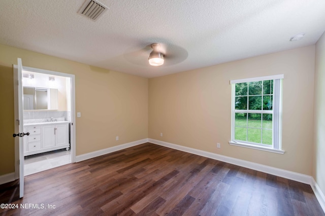 unfurnished bedroom with ceiling fan, a textured ceiling, ensuite bath, and dark wood-type flooring