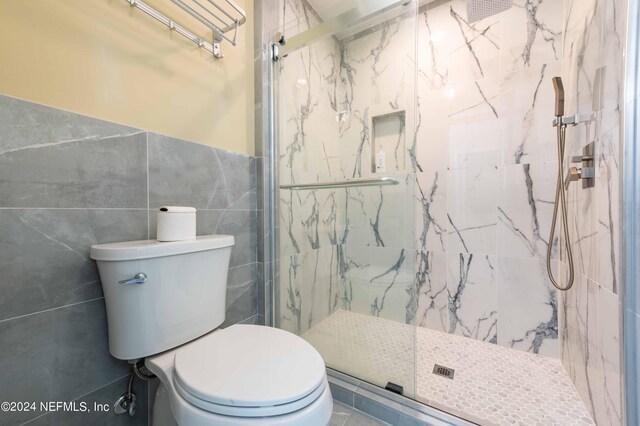 bathroom featuring toilet, a shower with door, and tile walls