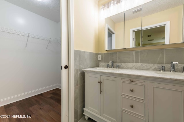 bathroom with hardwood / wood-style flooring, tile walls, vanity, and a textured ceiling