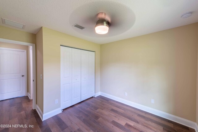 unfurnished bedroom with ceiling fan, dark hardwood / wood-style floors, a closet, and a textured ceiling