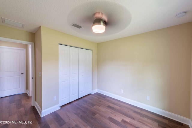 unfurnished bedroom with a textured ceiling, a closet, dark hardwood / wood-style floors, and ceiling fan