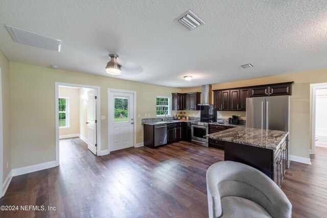 kitchen featuring sink, dark wood-type flooring, wall chimney exhaust hood, light stone countertops, and stainless steel appliances