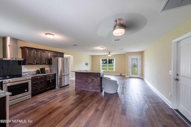 kitchen with appliances with stainless steel finishes, light stone counters, a kitchen island, dark hardwood / wood-style flooring, and wall chimney exhaust hood