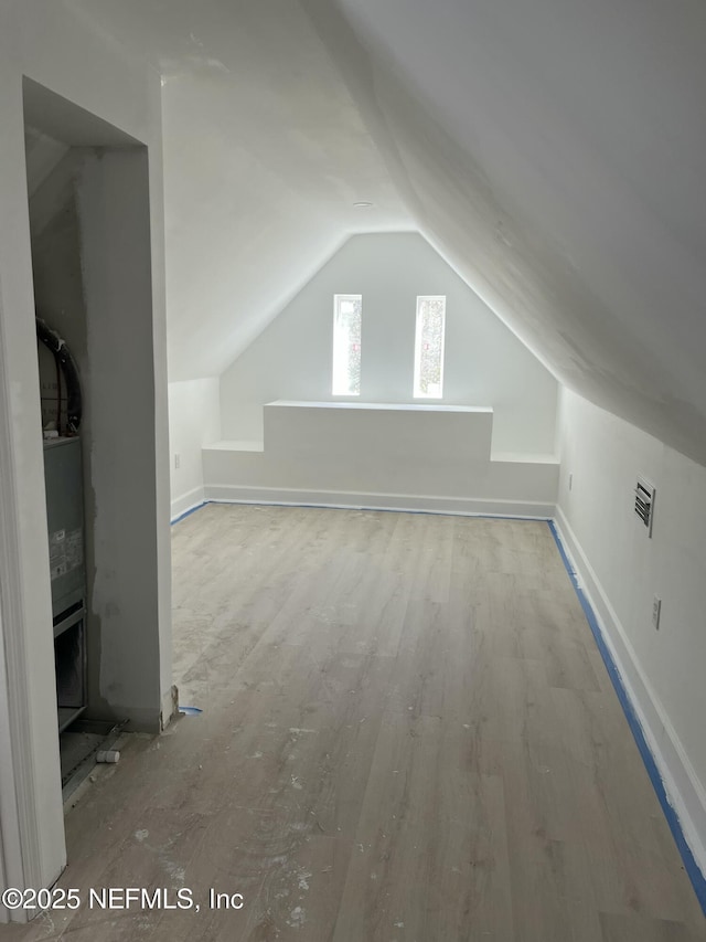 bonus room with light wood-style floors, baseboards, visible vents, and vaulted ceiling