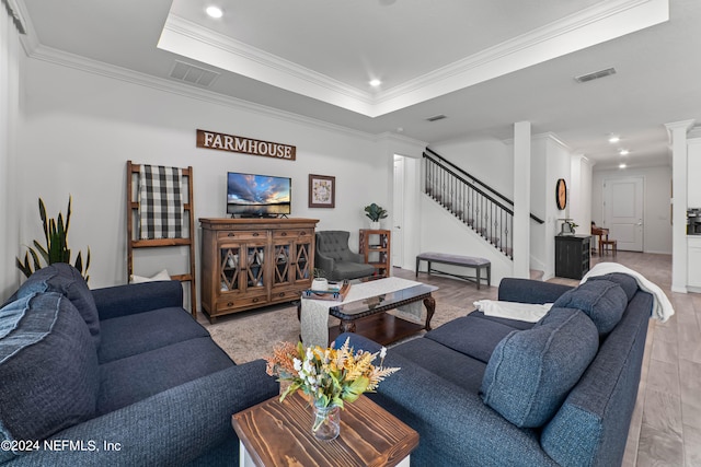 living room featuring light hardwood / wood-style floors, crown molding, a raised ceiling, and decorative columns