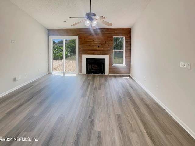 unfurnished living room with ceiling fan, wood-type flooring, a textured ceiling, and wooden walls