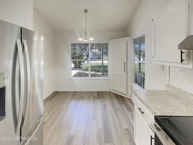 kitchen with light wood-type flooring, vaulted ceiling, stainless steel fridge, and decorative backsplash