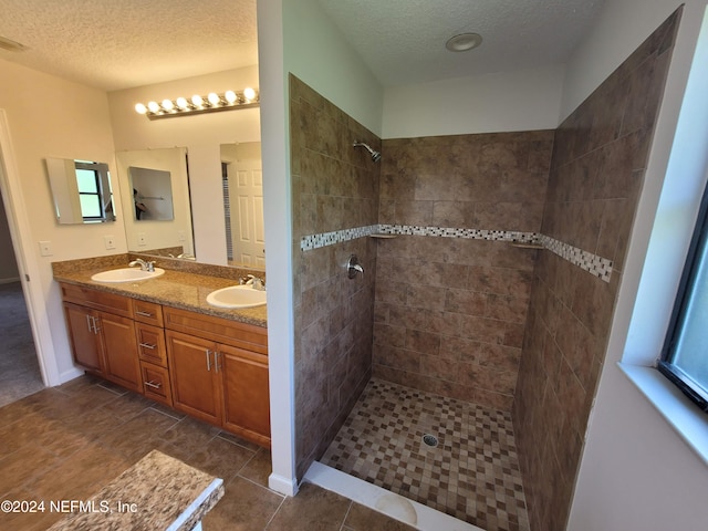 bathroom featuring a textured ceiling, tiled shower, vanity, and tile patterned floors