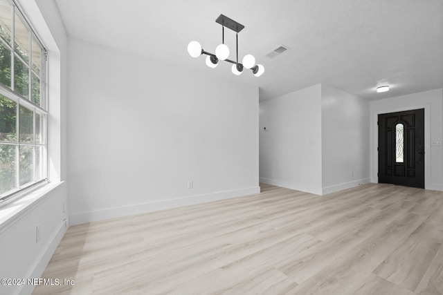 spare room featuring a chandelier, a textured ceiling, and light hardwood / wood-style flooring