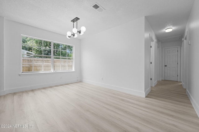 unfurnished room featuring a chandelier, a textured ceiling, and light wood-type flooring