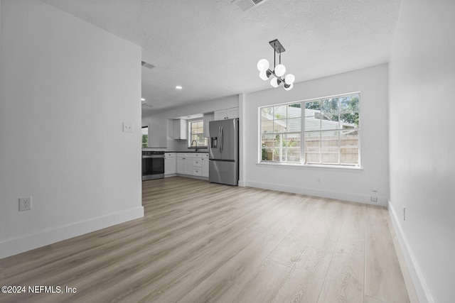 unfurnished living room with light hardwood / wood-style floors, a notable chandelier, a textured ceiling, and sink