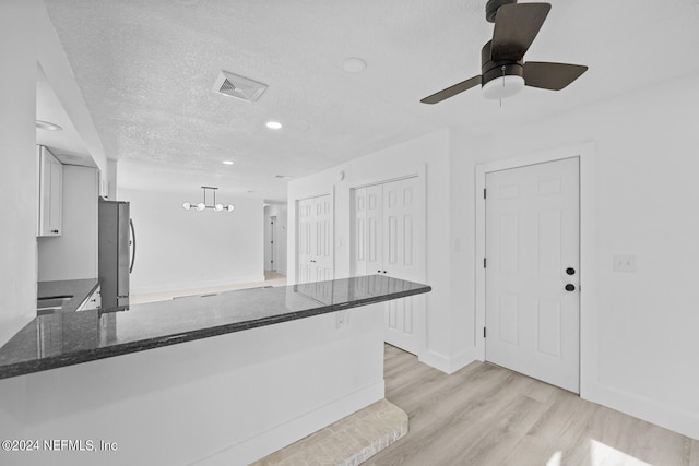 kitchen featuring stainless steel refrigerator, white cabinetry, a textured ceiling, decorative light fixtures, and light hardwood / wood-style flooring