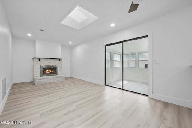 unfurnished living room with a fireplace, a textured ceiling, light hardwood / wood-style floors, a skylight, and ceiling fan