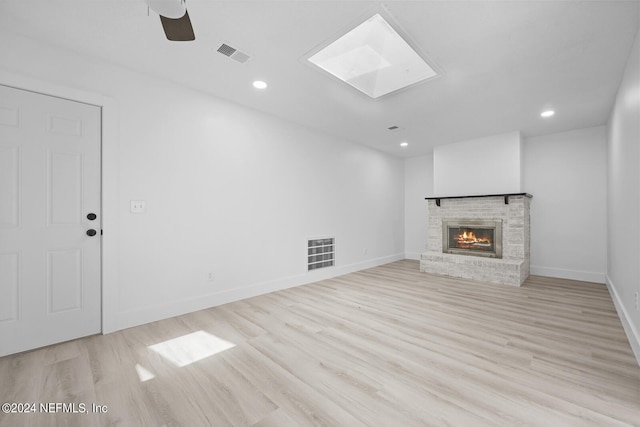 unfurnished living room with a fireplace, light hardwood / wood-style floors, ceiling fan, and a skylight