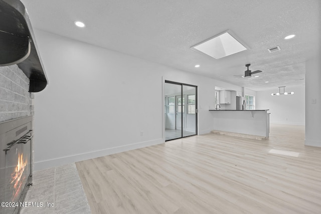 unfurnished living room featuring light hardwood / wood-style floors, a textured ceiling, a skylight, and ceiling fan