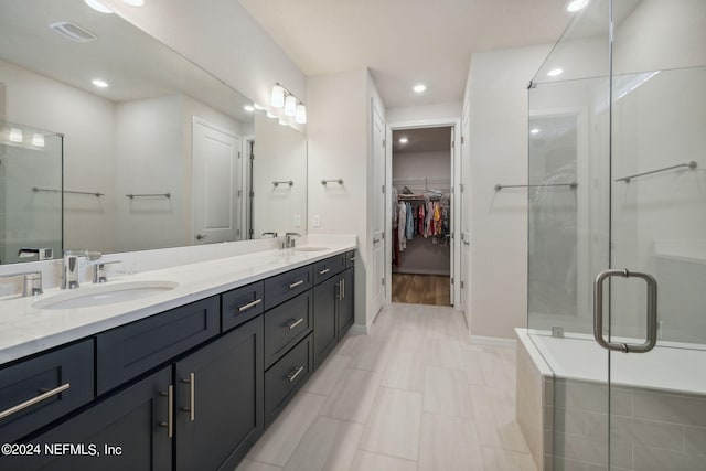 full bathroom with double vanity, a spacious closet, a sink, and a shower stall