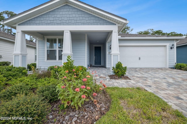 view of front of home with covered porch, decorative driveway, and an attached garage