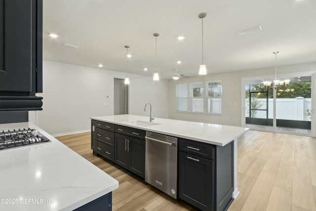 kitchen featuring light wood-style flooring, stainless steel appliances, a sink, a center island with sink, and pendant lighting