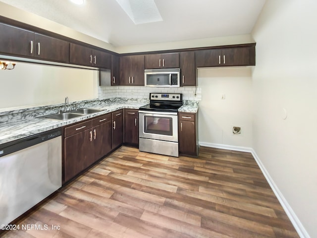 kitchen featuring light wood-type flooring, decorative backsplash, a skylight, sink, and stainless steel appliances