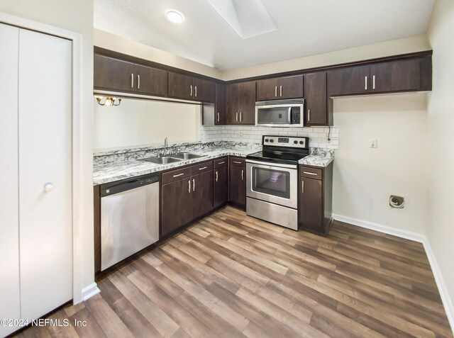 kitchen featuring hardwood / wood-style flooring, decorative backsplash, a skylight, sink, and stainless steel appliances