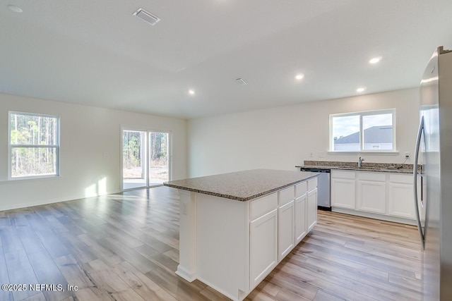 kitchen with white cabinetry, a center island, light wood-type flooring, dark stone countertops, and stainless steel appliances