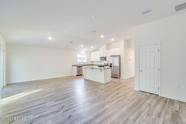 kitchen featuring appliances with stainless steel finishes, a breakfast bar, white cabinets, a center island, and light hardwood / wood-style flooring