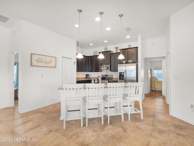 kitchen with stainless steel appliances, dark brown cabinetry, a kitchen breakfast bar, light tile patterned flooring, and hanging light fixtures