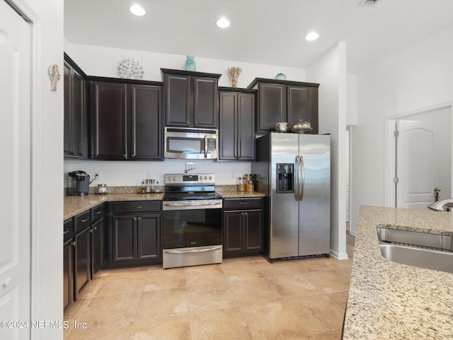 kitchen featuring appliances with stainless steel finishes, light stone counters, sink, light tile patterned flooring, and dark brown cabinets