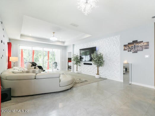 tiled living room featuring a raised ceiling and an inviting chandelier