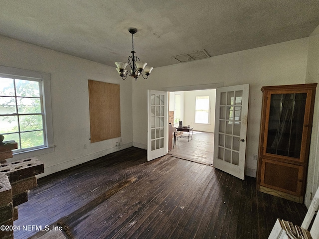 unfurnished dining area with a healthy amount of sunlight, a notable chandelier, dark wood-type flooring, and french doors