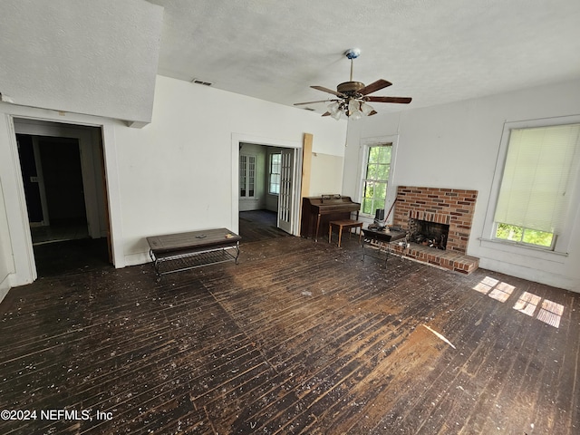 unfurnished living room with a textured ceiling, ceiling fan, a fireplace, visible vents, and hardwood / wood-style floors
