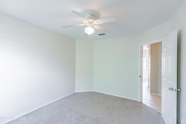 carpeted spare room featuring ceiling fan, visible vents, baseboards, and tile patterned floors