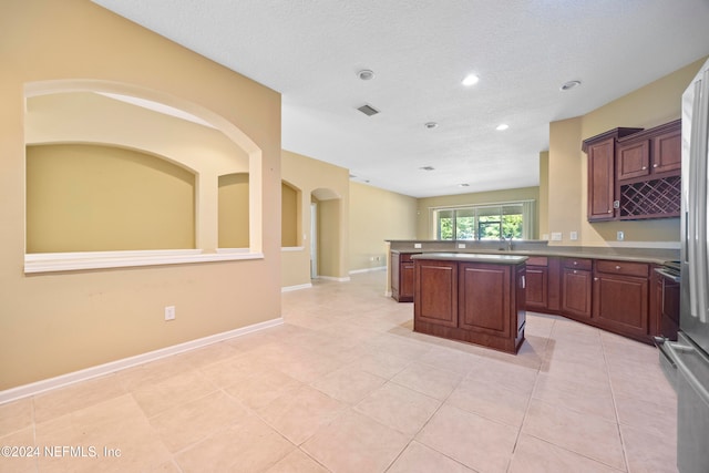 kitchen with kitchen peninsula, a kitchen island, light tile patterned flooring, and a textured ceiling