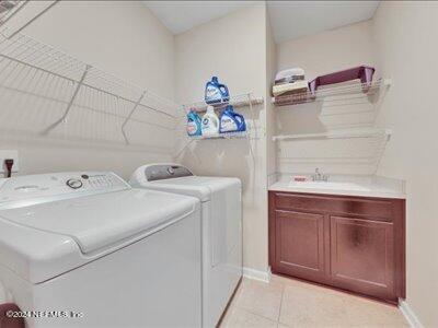 laundry area featuring light tile patterned flooring, washing machine and dryer, baseboards, and a sink