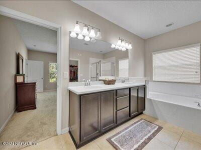 bathroom with tile patterned flooring, separate shower and tub, an inviting chandelier, and dual vanity