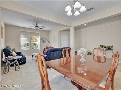 carpeted dining space with ceiling fan with notable chandelier