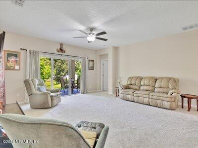 living area featuring carpet flooring, a textured ceiling, visible vents, and a ceiling fan