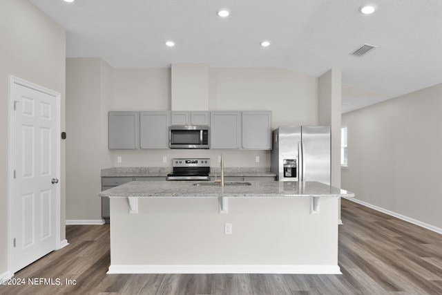 kitchen featuring wood-type flooring, stainless steel appliances, a center island with sink, and light stone countertops